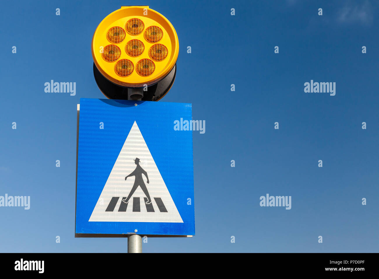 Attraversamento pedonale. Quadrato blu e bianco cartello stradale con schemi uomo a piedi e giallo di avvertimento luci nel cielo blu sullo sfondo Foto Stock