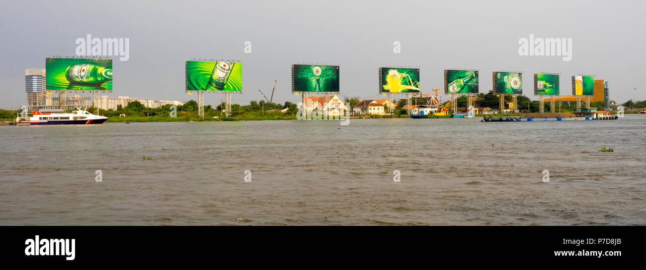 Trasporto alla rinfusa chiatta trasporta un carico e il traghetto sul fiume Saigon con la mitica Heineken cartelloni in background., Ho Chi Minh City, Vietnam. Foto Stock