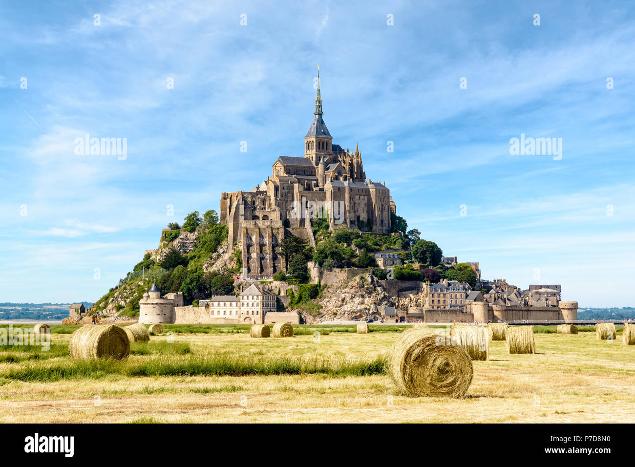 Il Mont Saint Michel isola di marea in Normandia, Francia, con le balle di paglia in un campo in primo piano sotto un cielo blu con nuvole fibroso. Foto Stock