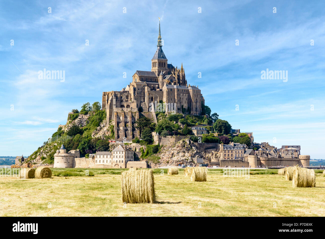 Il Mont Saint Michel isola di marea in Normandia, Francia, con le balle di paglia in un campo in primo piano sotto un cielo blu con nuvole fibroso. Foto Stock
