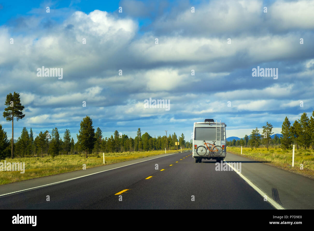 Veicolo ricreativo con bici appese sulla parte posteriore di guida attraverso la campagna. Viaggi e wanderlust Concetto di immagine con una copia dello spazio. Foto Stock