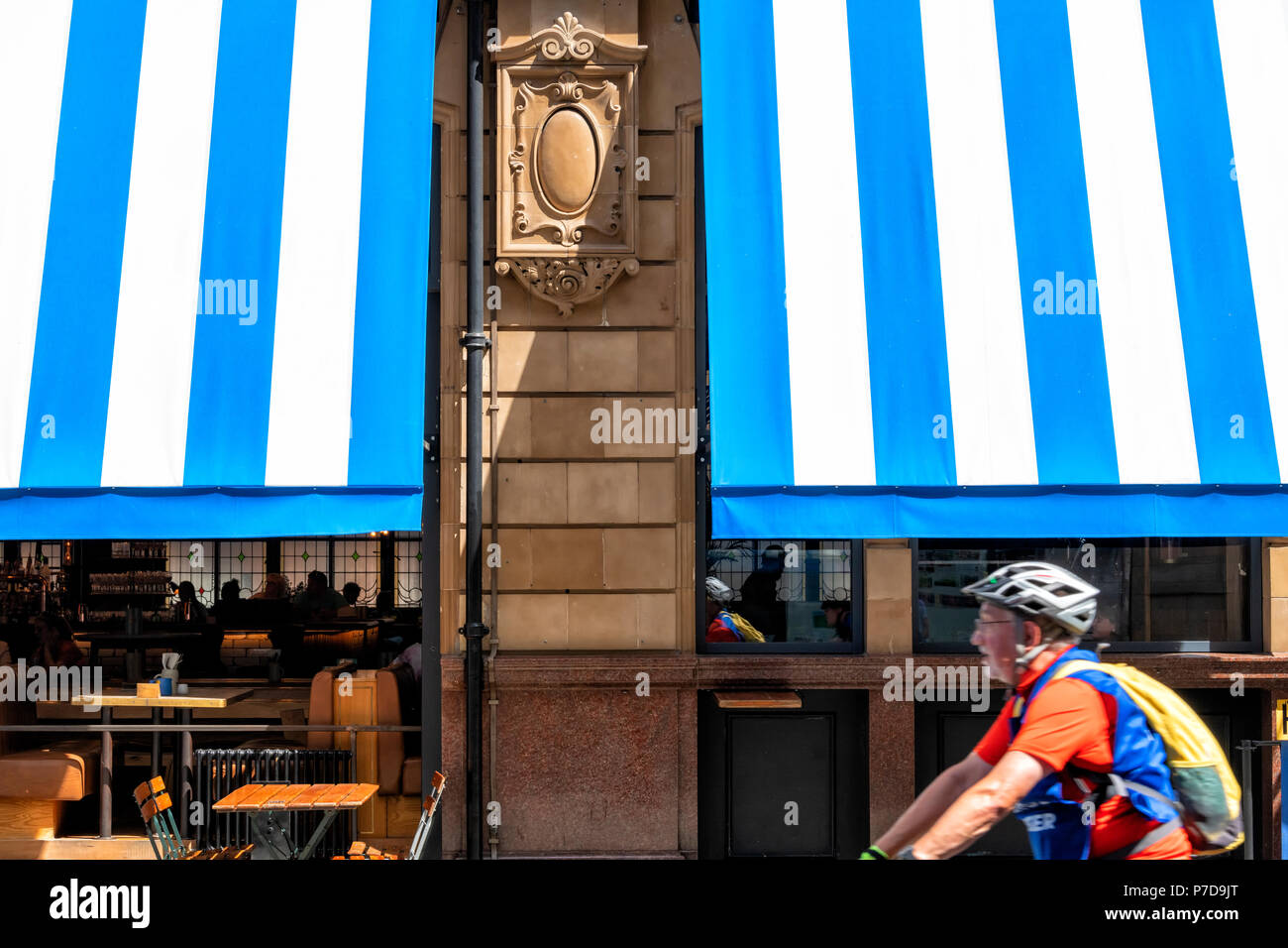 Un ciclista passa il suggestivo blu e bianco tende a strisce sulla parte anteriore del Albert ristorante Schloss in Manchester City Centre Foto Stock