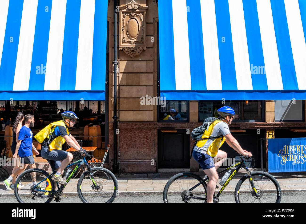 A pedoni e ciclisti passare il suggestivo blu e bianco tende a strisce sulla parte anteriore del Albert ristorante Schloss in Manchester City Centre Foto Stock