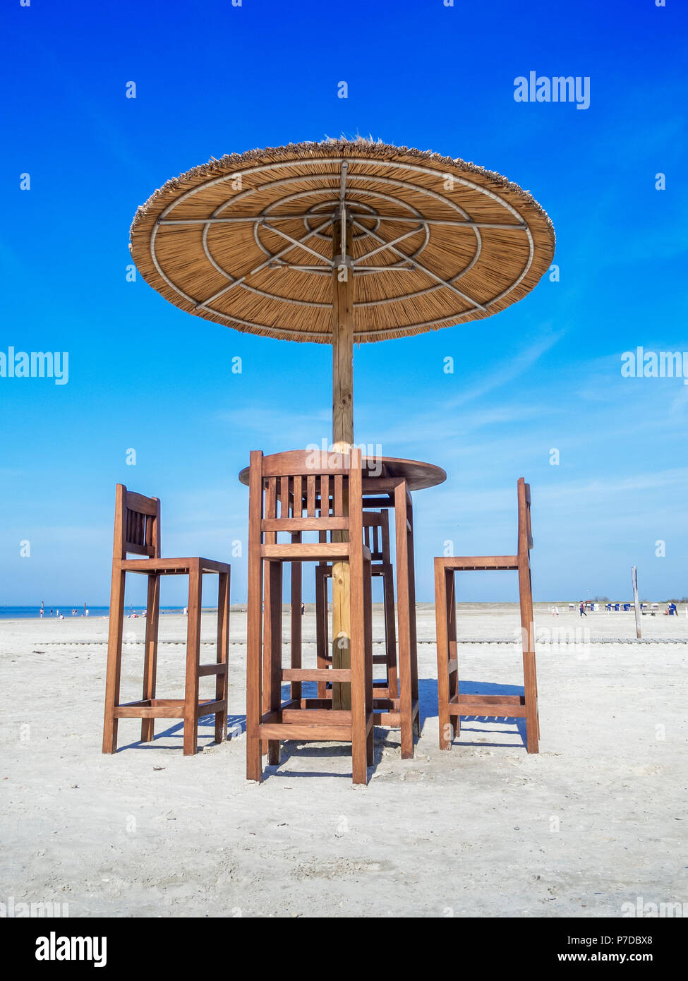 Vista profonda sulla spiaggia un tavolo con quattro sedie per bar e reed ombrellone sulla spiaggia il cielo blu con nuvole. Foto Stock