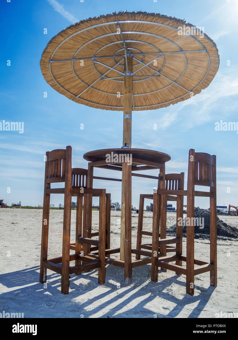 Vista profonda sulla spiaggia un tavolo con quattro sedie per bar e canne ombrellone sulla spiaggia di cielo blu con nuvole. Foto Stock