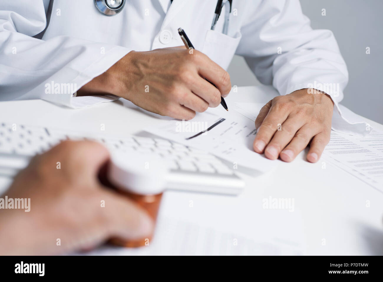 Primo piano di un medico caucasica uomo in camice bianco, firma una prescrizione per un senior caucasica uomo paziente che hanno una bottiglia di pillole in mano, s Foto Stock