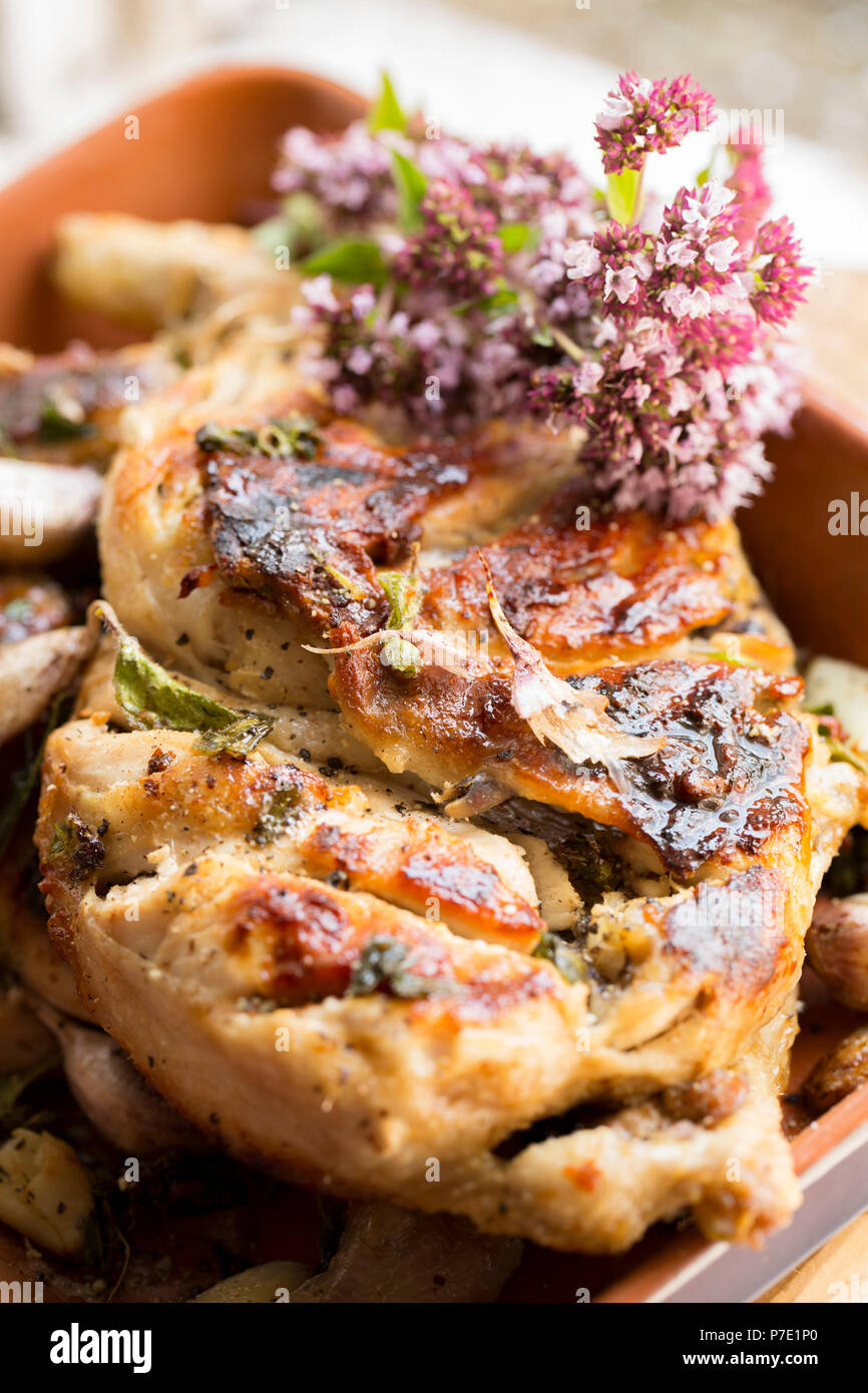 Un pollo intero che è stata dimezzata e grigliati con interi gli spicchi d aglio e origano, Origanum vulgare. Servite con una decorazione di un mazzetto di Wil Foto Stock