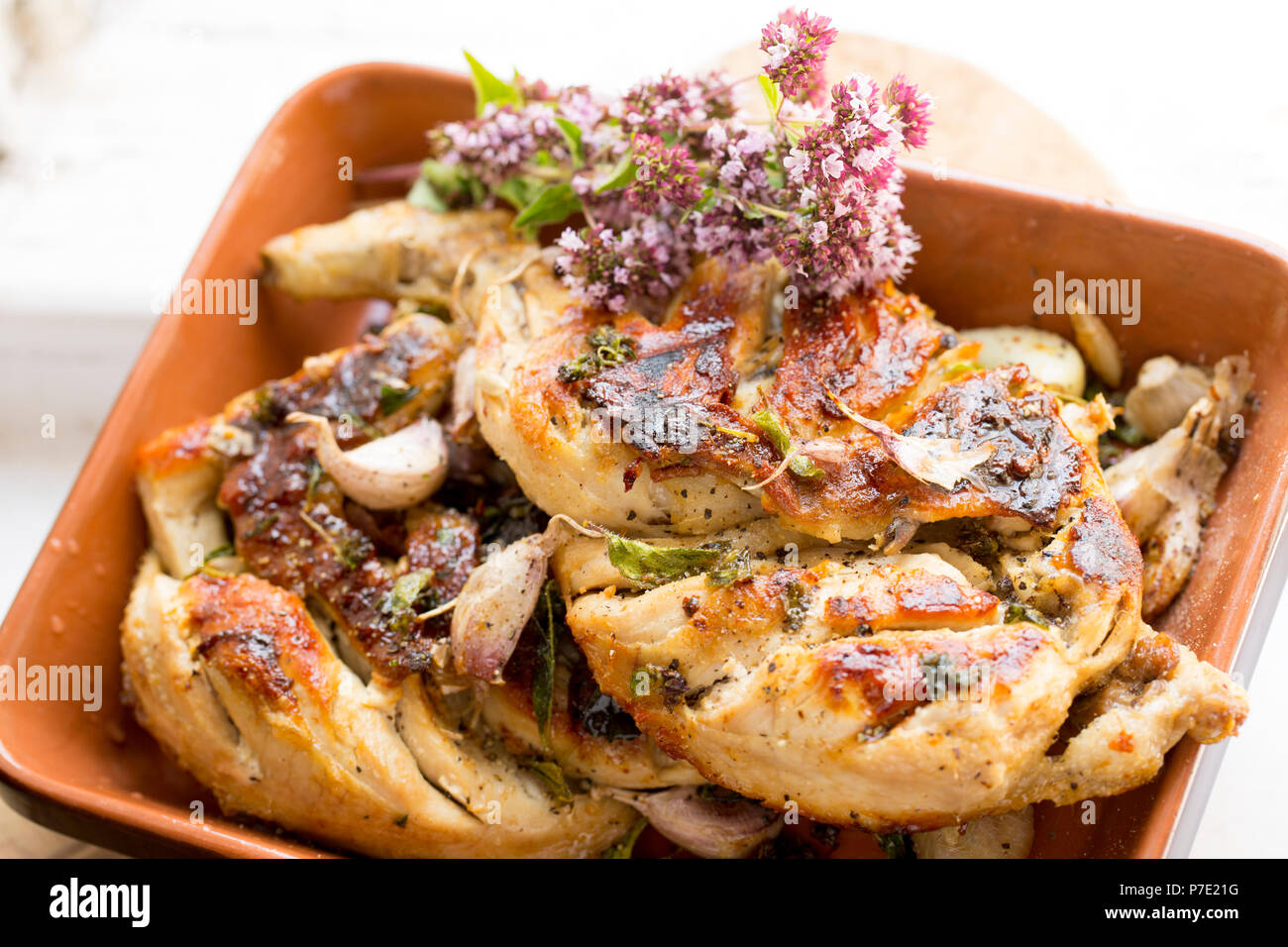 Un pollo intero che è stata dimezzata e grigliati con interi gli spicchi d aglio e origano, Origanum vulgare. Servite con una decorazione di un mazzetto di Wil Foto Stock