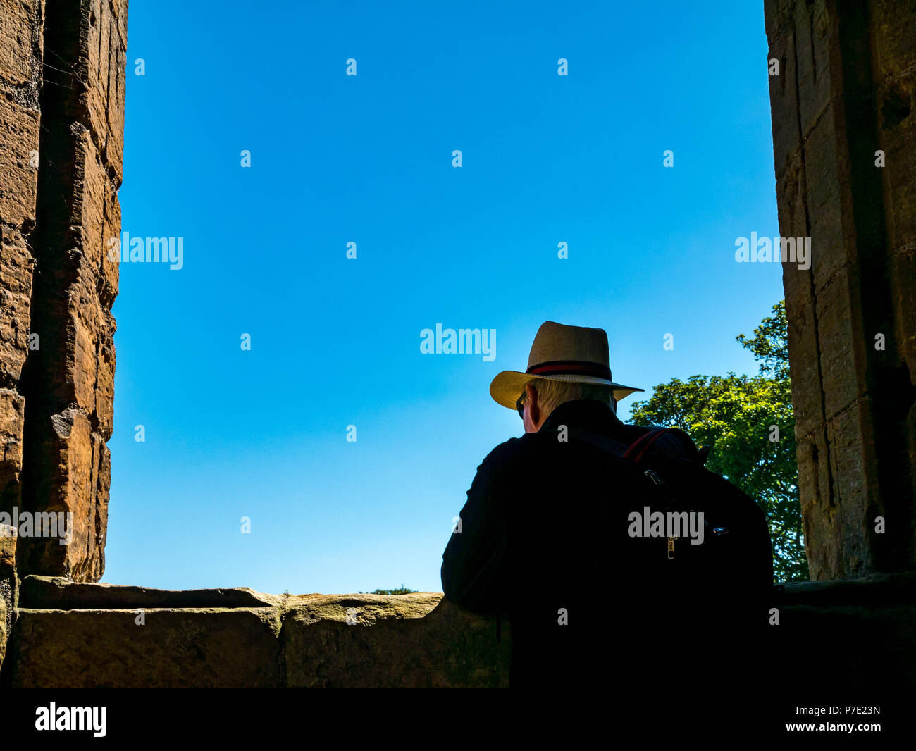 Incorniciato silhouette di un uomo che indossa cappello di Panama in rovina il telaio del finestrino con cielo blu, Linlithgow Palace, West Lothian, Scozia, Regno Unito Foto Stock