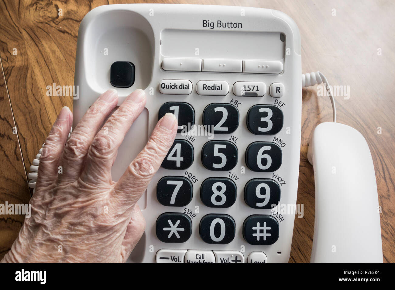 Ipovedenti donna anziana componendo NHS 111 linea guida sul grande pulsante telefono. Foto Stock