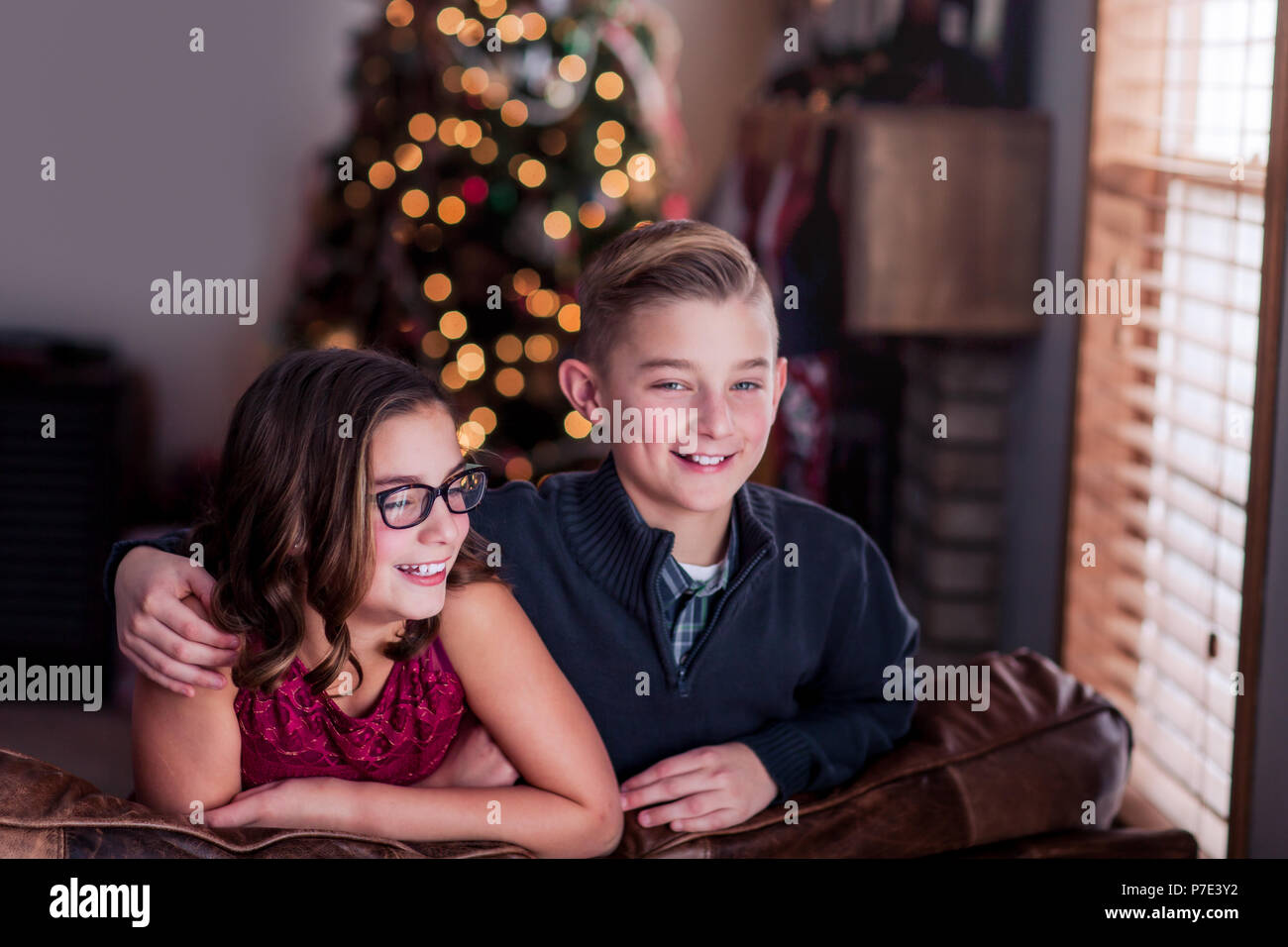 I fratelli sporgendoti divano, sorridente, albero di Natale in background Foto Stock