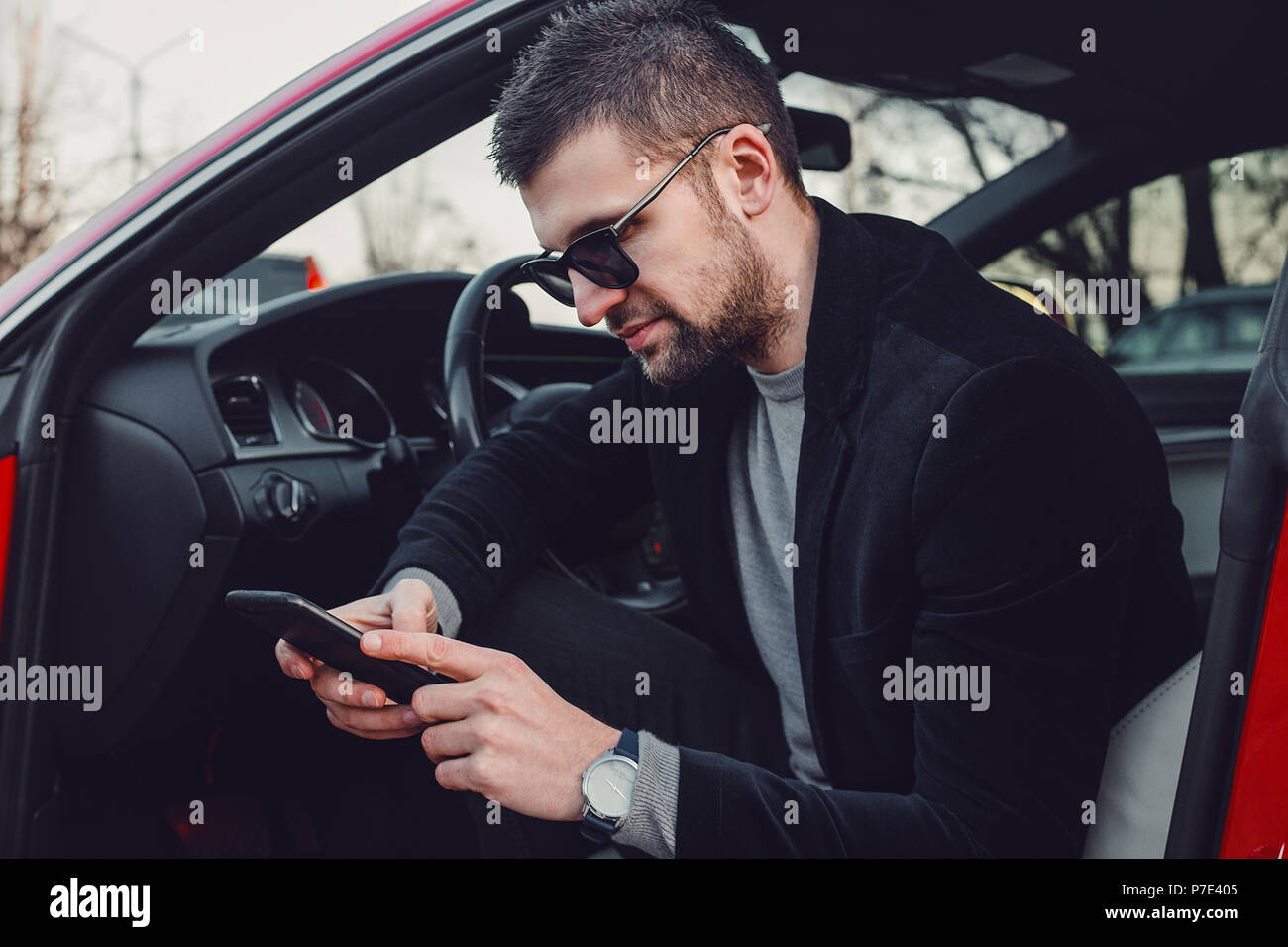 Imprenditore barbuto utilizzando il telefono cellulare in auto di lusso Foto Stock