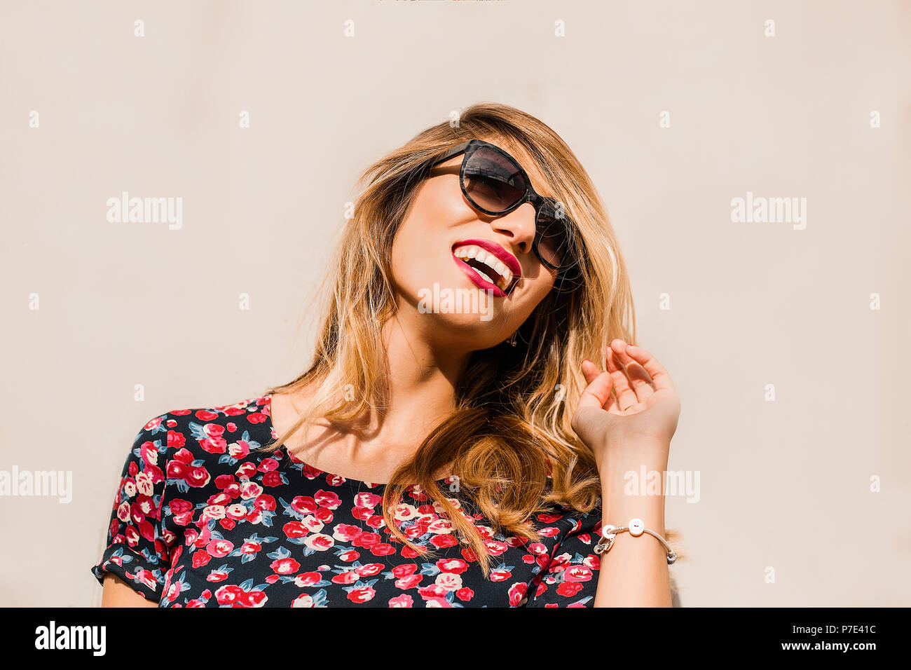 Bionda, elegante metà donna adulta indossando occhiali da sole nella parte anteriore della parete di ridere Foto Stock