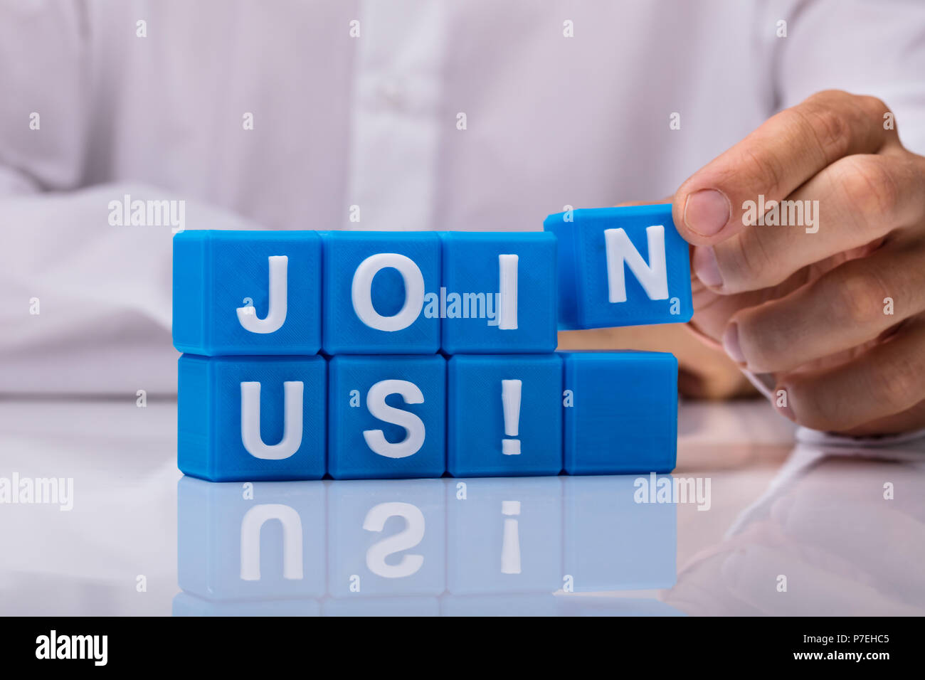 Mano umana edificio blu blocchi cubici con Unisciti a noi il testo sulla scrivania riflettente Foto Stock