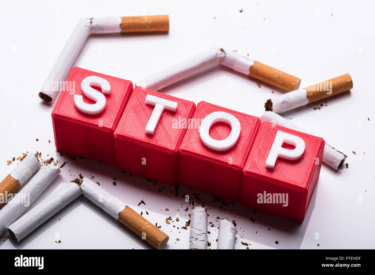 Rosso di arresto blocchi cubici circondato da rotture di sigarette su sfondo bianco Foto Stock