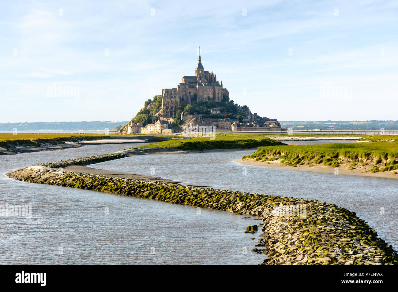 Vista del Mont Saint Michel isola di marea in Normandia, Francia, a marea alta con una diga di pietra sul fiume Couesnon in primo piano. Foto Stock