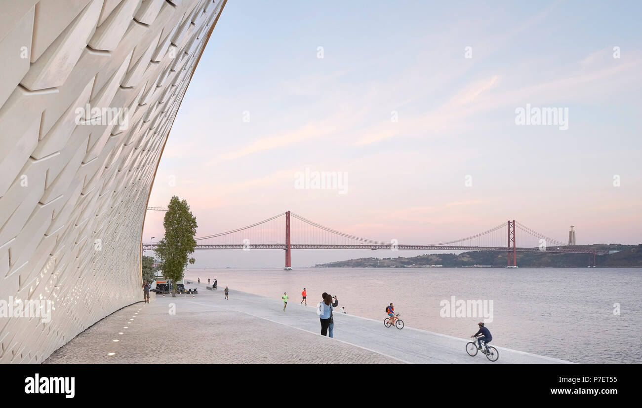 Passi sul lungomare e sinuosa facciata con pista ciclabile e la vista del ponte. MAAT, Lisbona, Portogallo. Architetto: UN LA, 2016. Foto Stock