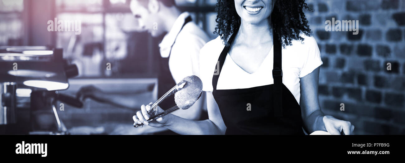 Sorridente cameriera mettendo panino nel sacchetto di carta Foto Stock