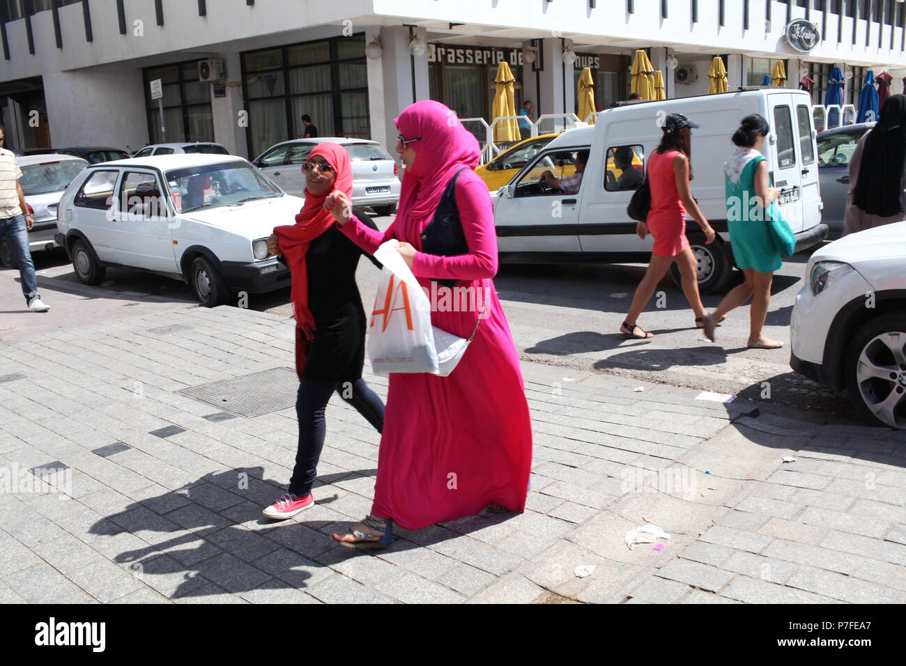 Il giorno moderno turista nel paese arabo, a Tunisi, Tunisia, due donne arabe in rosa abiti musulmani sono a piedi mentre in background di due donne straniere andare Foto Stock