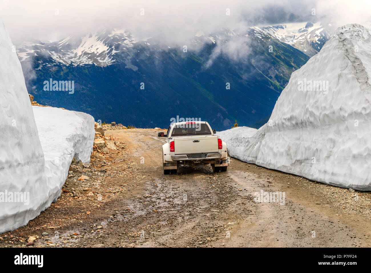 La vettura si muove su un umido, pietroso, sporcizia, strada di montagna, tra cumuli di neve, precedendo la cima di una montagna coperta da una fitta nebbia di bianco Foto Stock