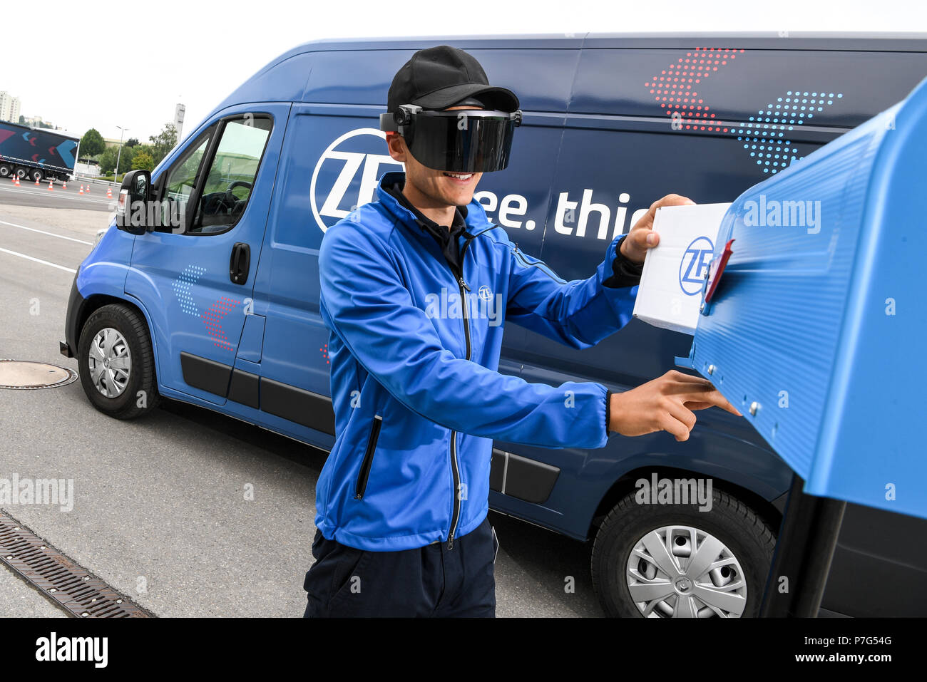 27 giugno 2018, Friedrichshafen, Germania: un dipendente ZF trasporta un pacchetto mentre l'innovazione ZF Van unità dalla stessa, ad esempio per spostare al di fuori di un no-zona parcheggio. Un paio di occhiali di dati fornisce il personale addetto alle consegne con informazioni sulla prossima fermata. Foto: Felix Kästle/dpa Foto Stock