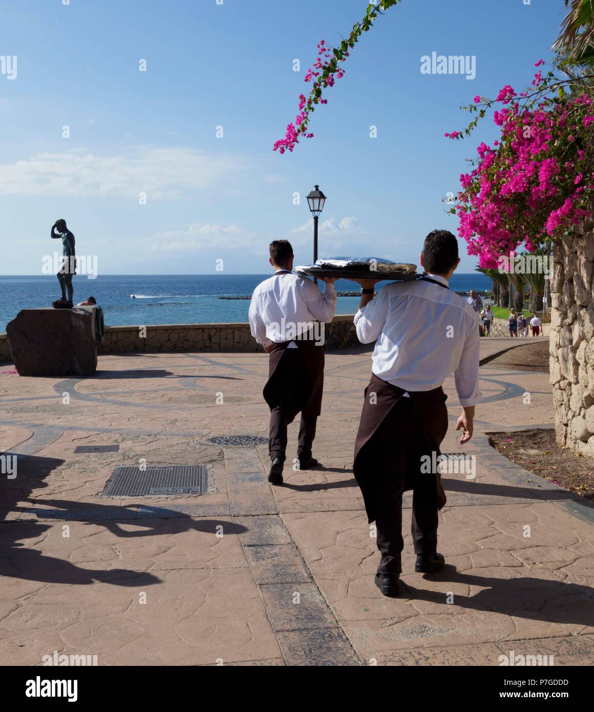 Tenerife, Isole Canarie - Bahia del Duque. I camerieri prendere pizze giù la passeggiata per la consegna di un appartamento. Foto Stock