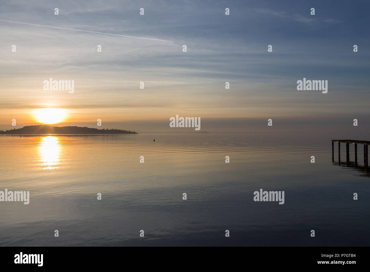 Una ripresa di un tramonto su un lago, con il sole che scende dietro un'isola e un molo sulla destra Foto Stock