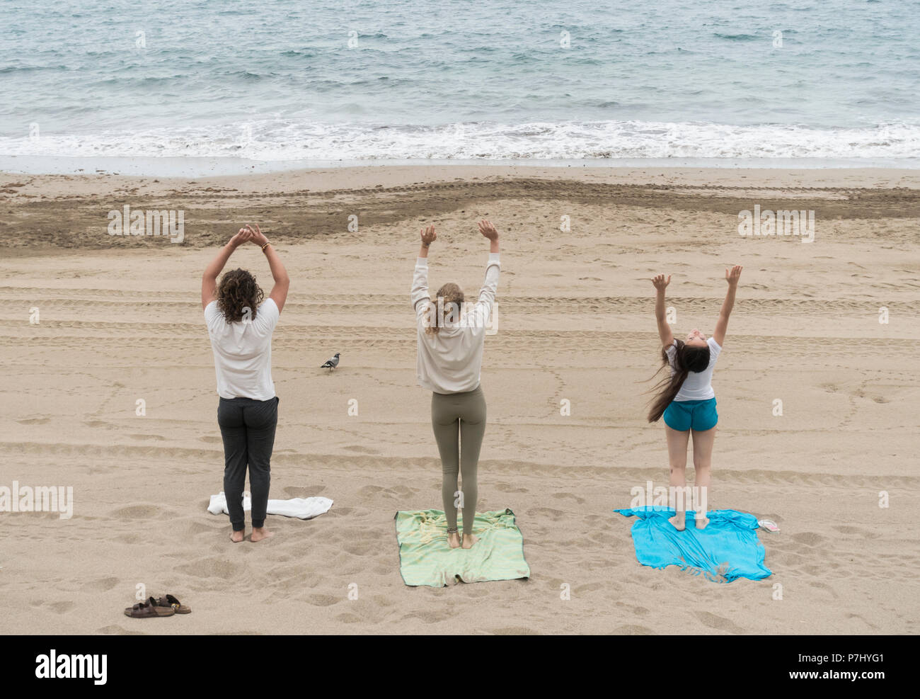 Tre giovani (due donne e un uomo) eseguendo lo Yoga con piccioni sulla spiaggia Foto Stock