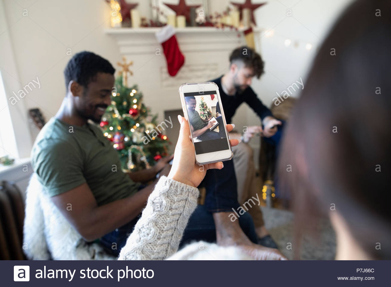 Giovane donna con la fotocamera del telefono a fotografare gli amici di Natale sale di soggiorno Foto Stock