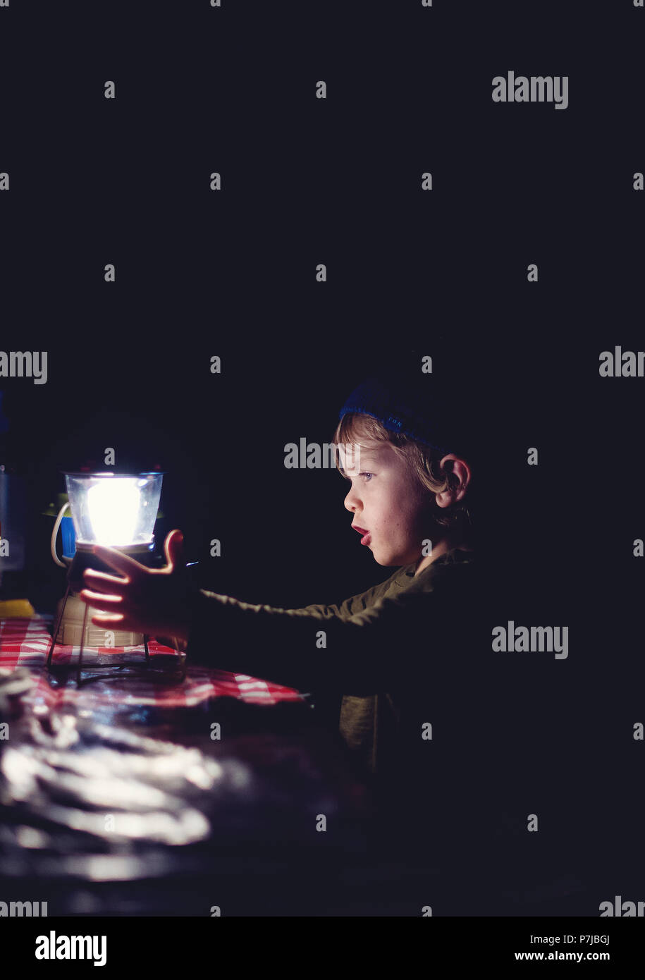 Ragazzo accanto a una lanterna su un tavolo a un campeggio Foto Stock