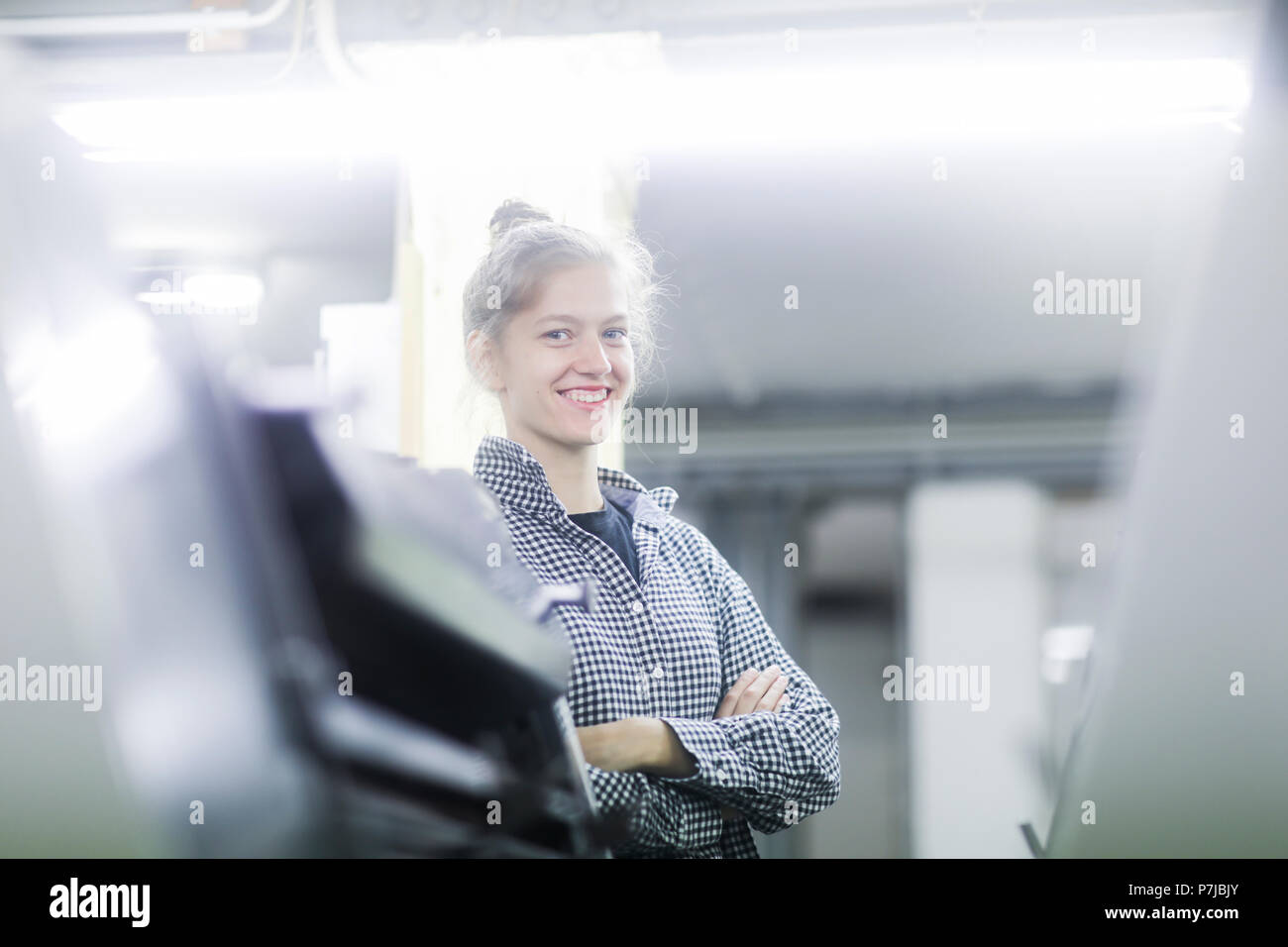 Donna sorridente in piedi in una fabbrica con le braccia piegate Foto Stock