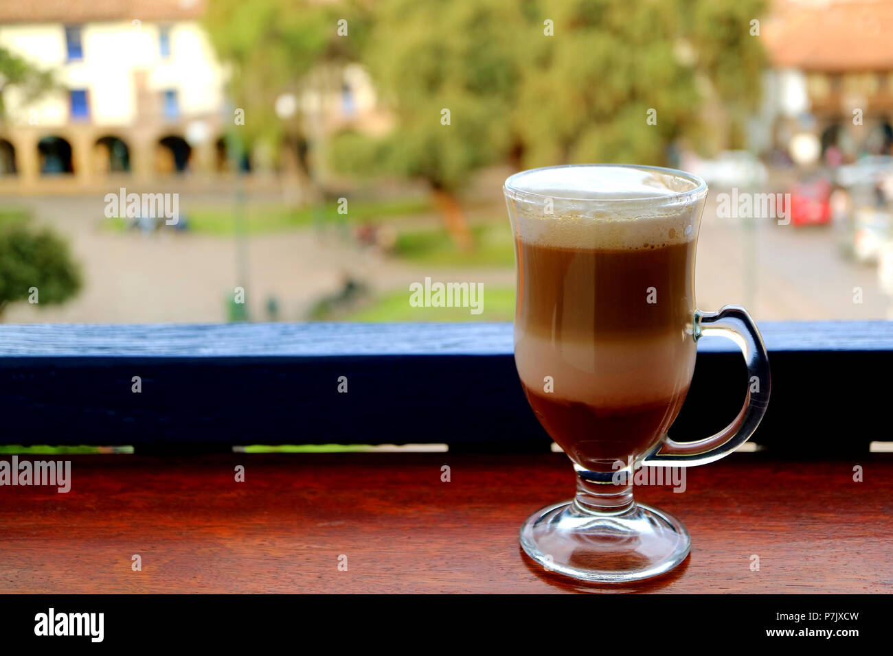 Cappuccino caldo il caffè in una coppa trasparente servita presso la terrazza con sfumata la piazza della città vecchia di Cusco, Perù in background Foto Stock
