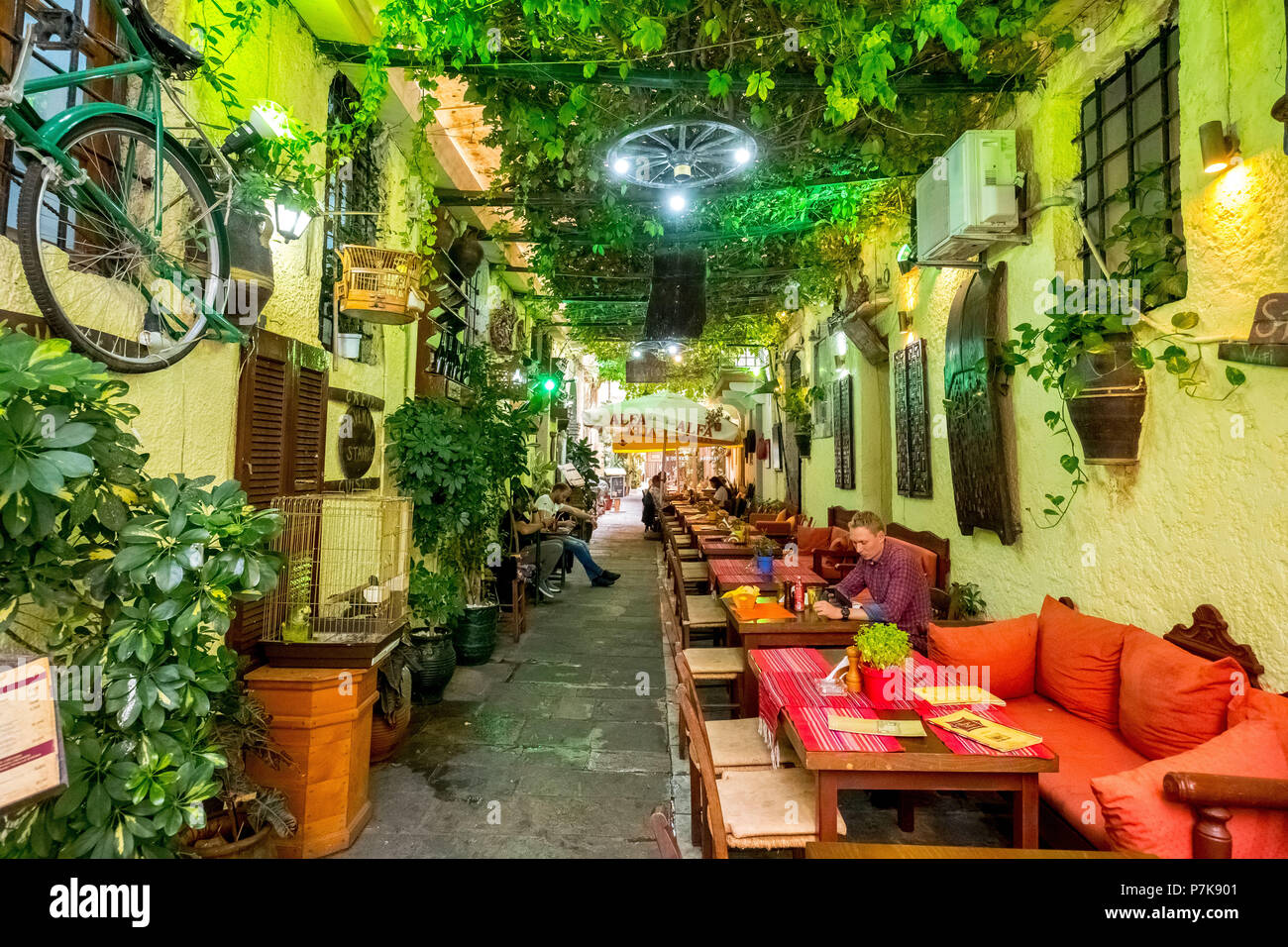Ristorante, taverna in un vicolo nella città vecchia di Rethymno, foglie di vite e divani rossi, Europa, Creta, Grecia Foto Stock