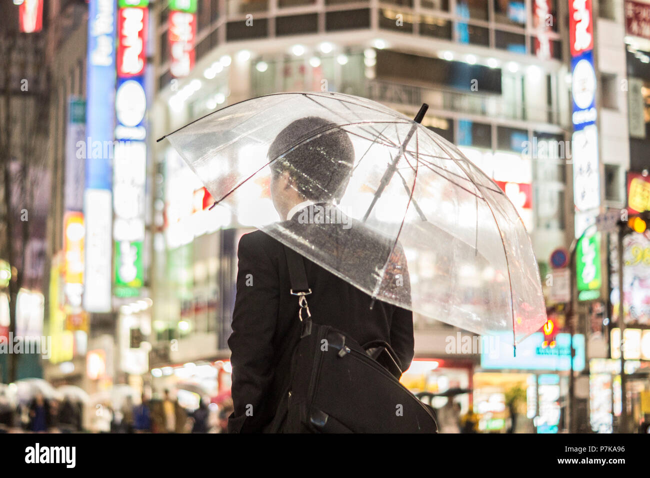 Un imprenditore con un ombrello in vivaci strade illuminate di sera Foto Stock
