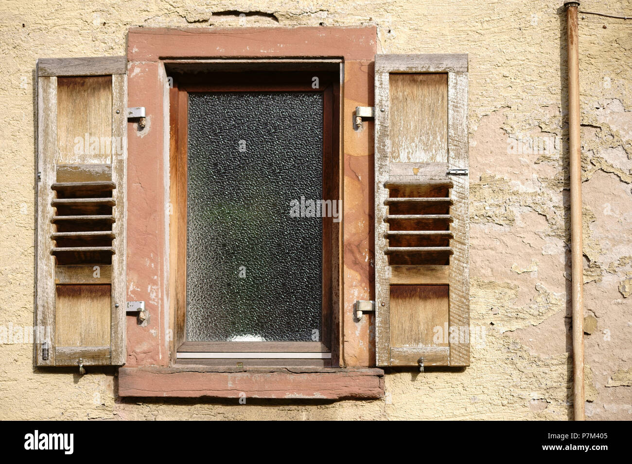 Una casa fatiscente con un ingiallito facciata e pareti scrostate e strati di gesso sulla finestra e persiane. Foto Stock