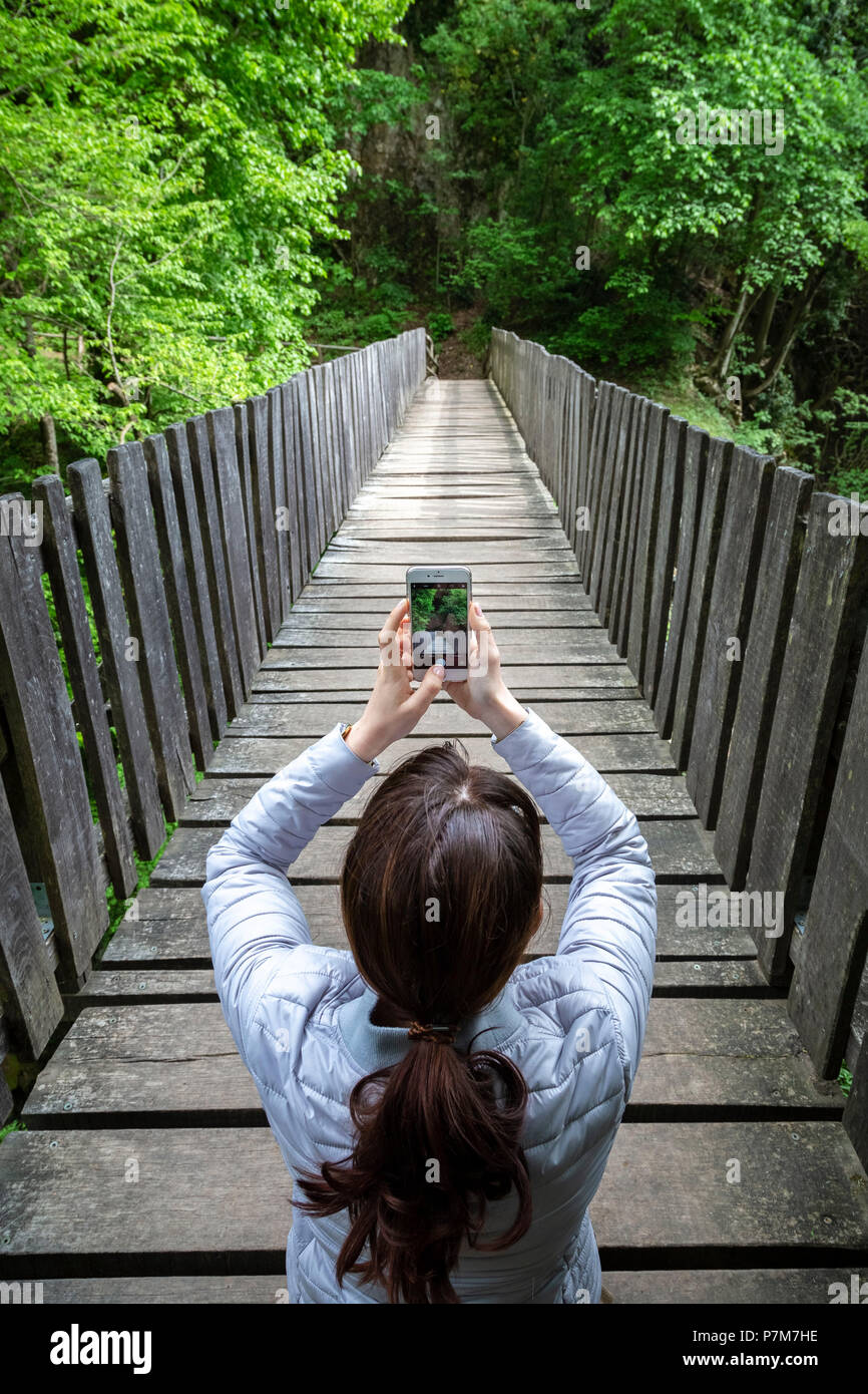 Una ragazza di scattare una foto su un ponte di legno sul sentiero della Breggia gole, Valle di Muggio, distretto di Mendrisio, Canton Ticino, Svizzera. Foto Stock