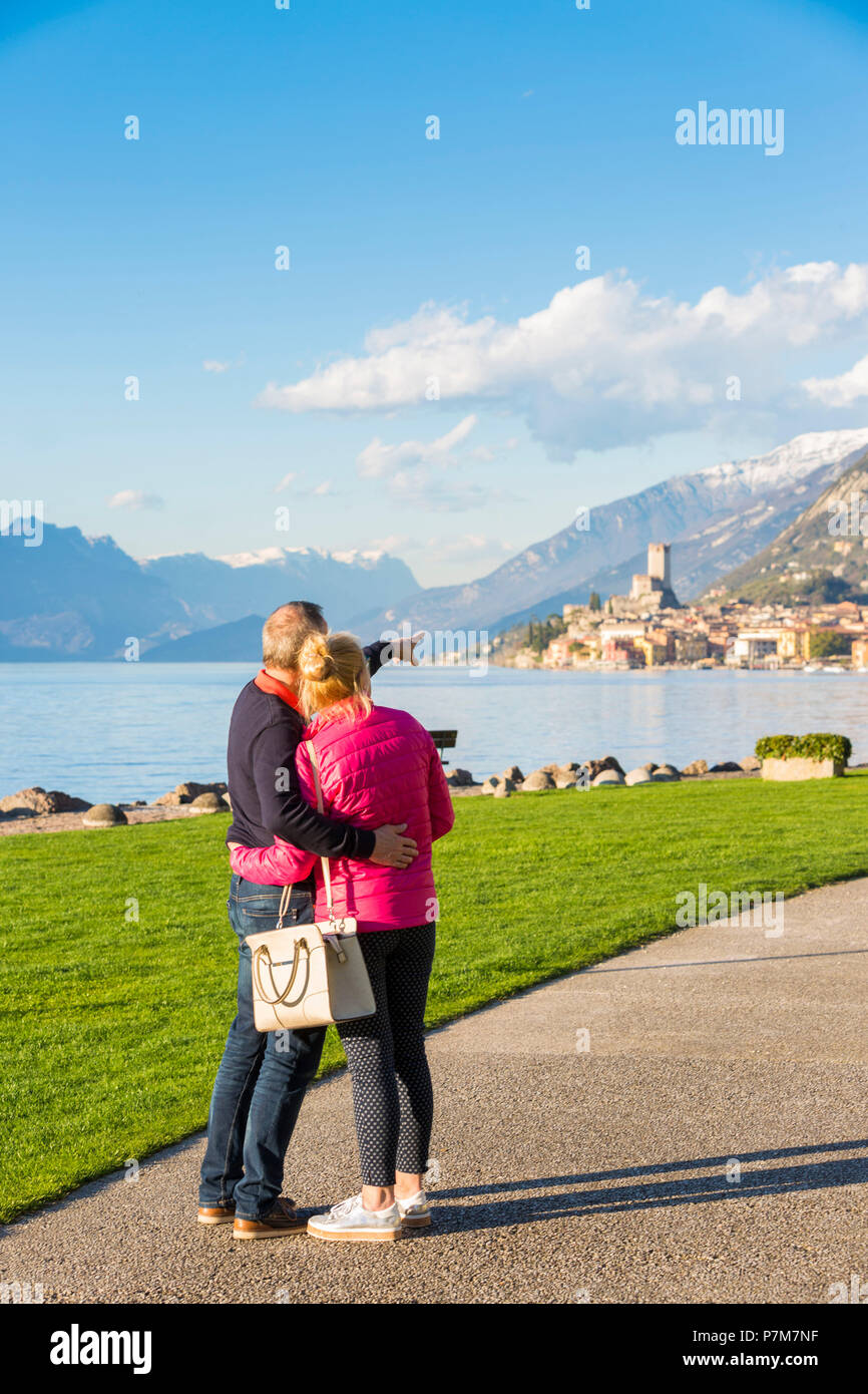 Un paio di turisti in ammirando Malcesine vista dal fronte del lago sulla sponda orientale del Lago di Garda, provincia di Verona, regione Veneto, Italia. Foto Stock