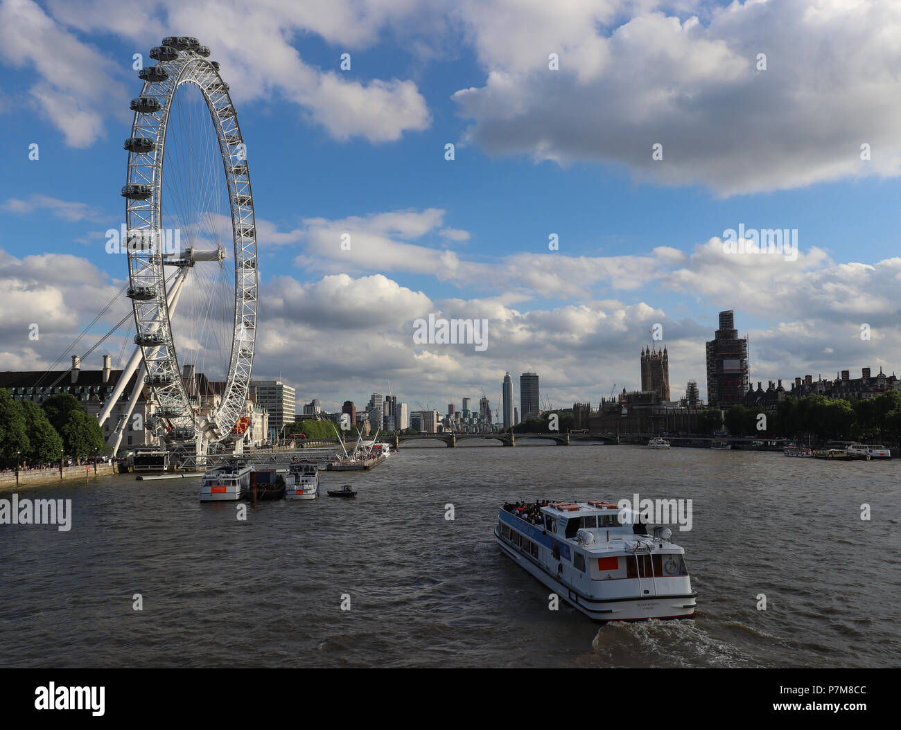 Visualizza in basso il fiume Tamigi del London Eye e le case del Parlamento con i ponteggi da Hungerford Bridge; blue sky riempito con il bianco delle nuvole Foto Stock