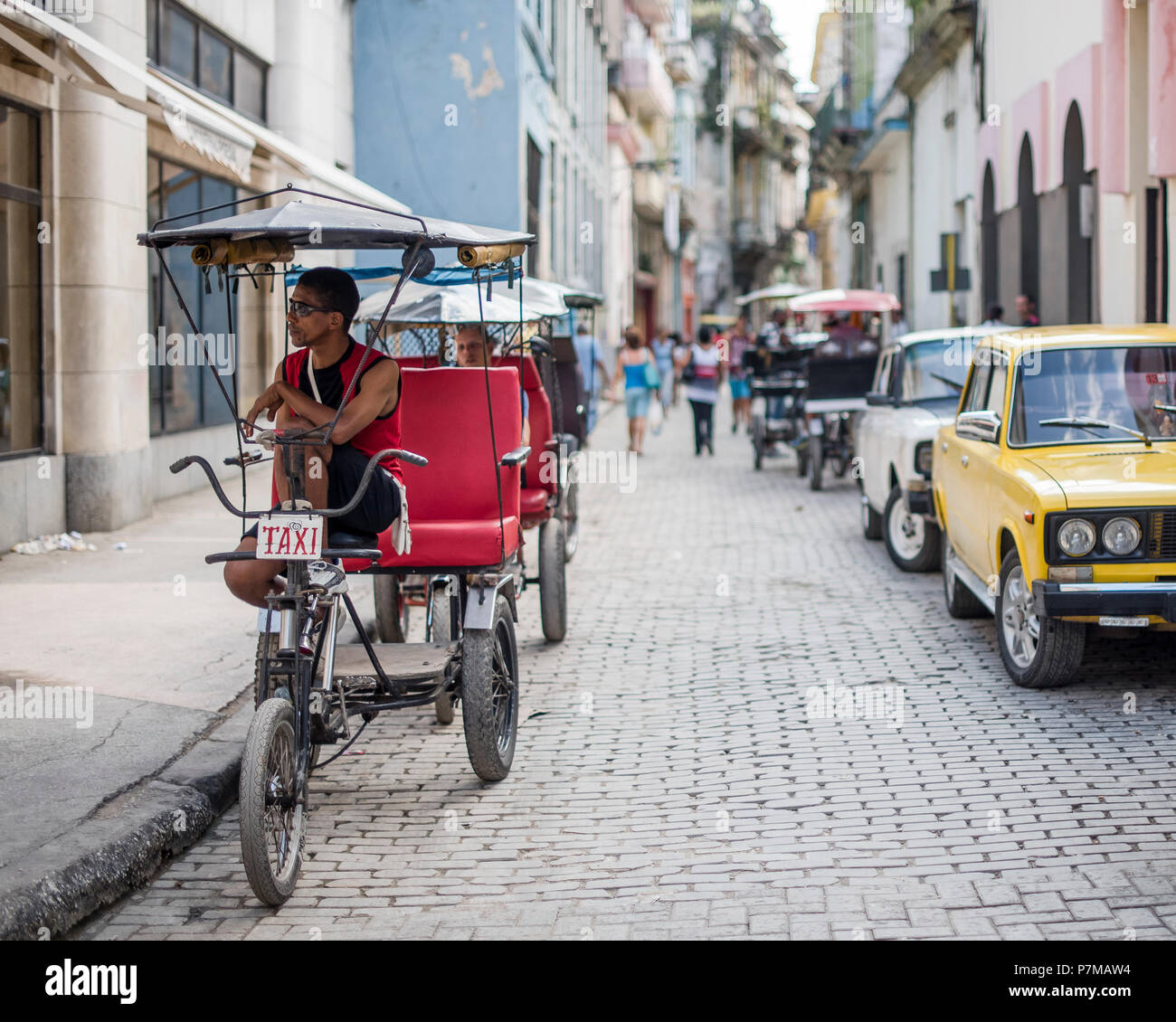 Una bicicletta cab driver attende il suo prossimo passeggero su una strada trafficata nella Vecchia Havana, Cuba. Foto Stock