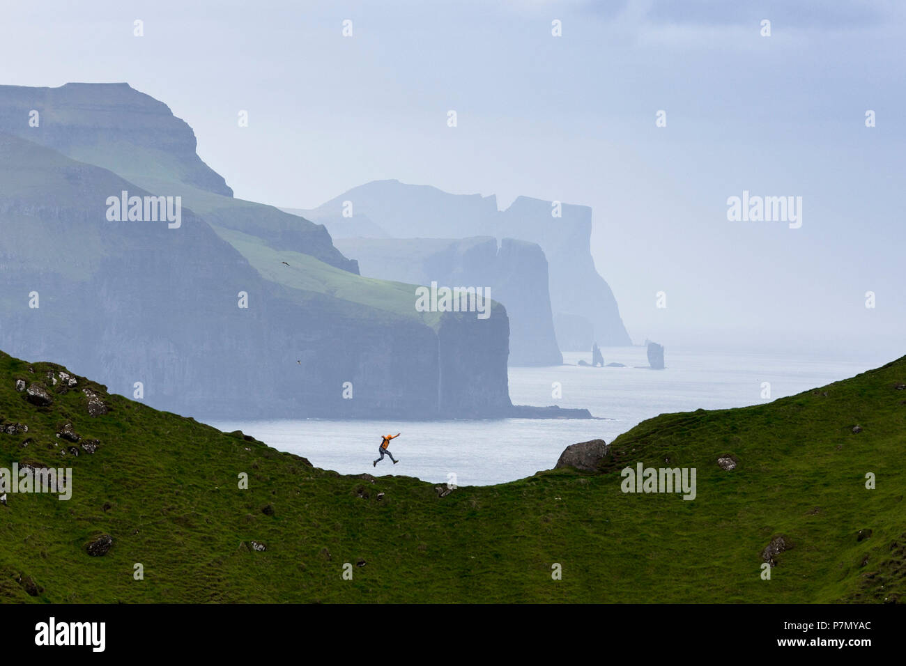 L'uomo saltando su scogliere, Kalsoy isola, isole Faerøer, Danimarca Foto Stock