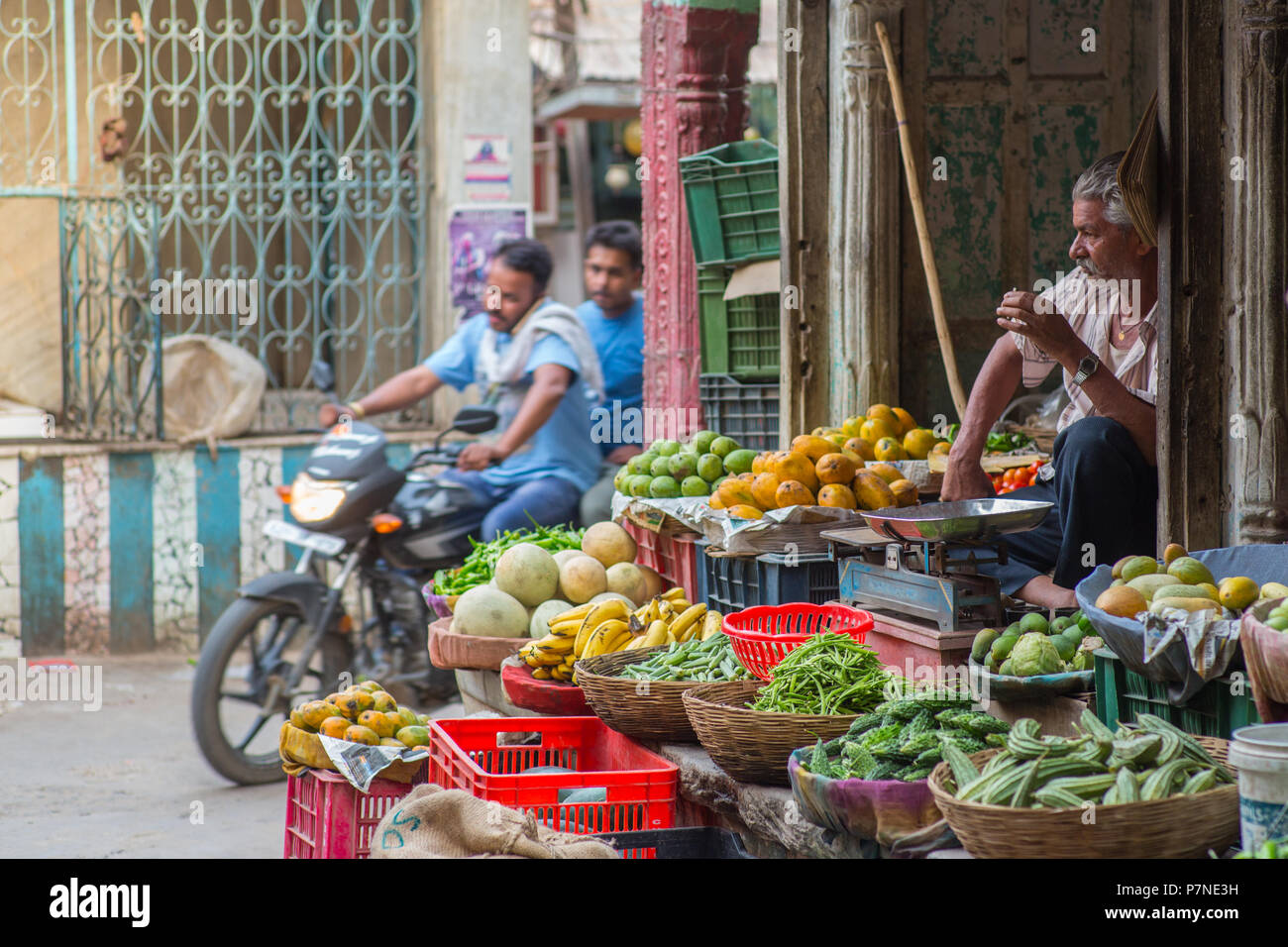 Locali di frutta e verdura seduta del fornitore su nel suo negozio in Pushkar, India, su una strada trafficata come un motociclo rigidi mediante. Foto Stock