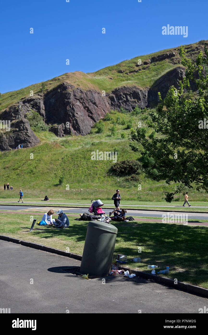 Rifiuti Cucciolata bin traboccante di turisti in background, Holyrood Park, Edimburgo, Scozia, Regno Unito Foto Stock