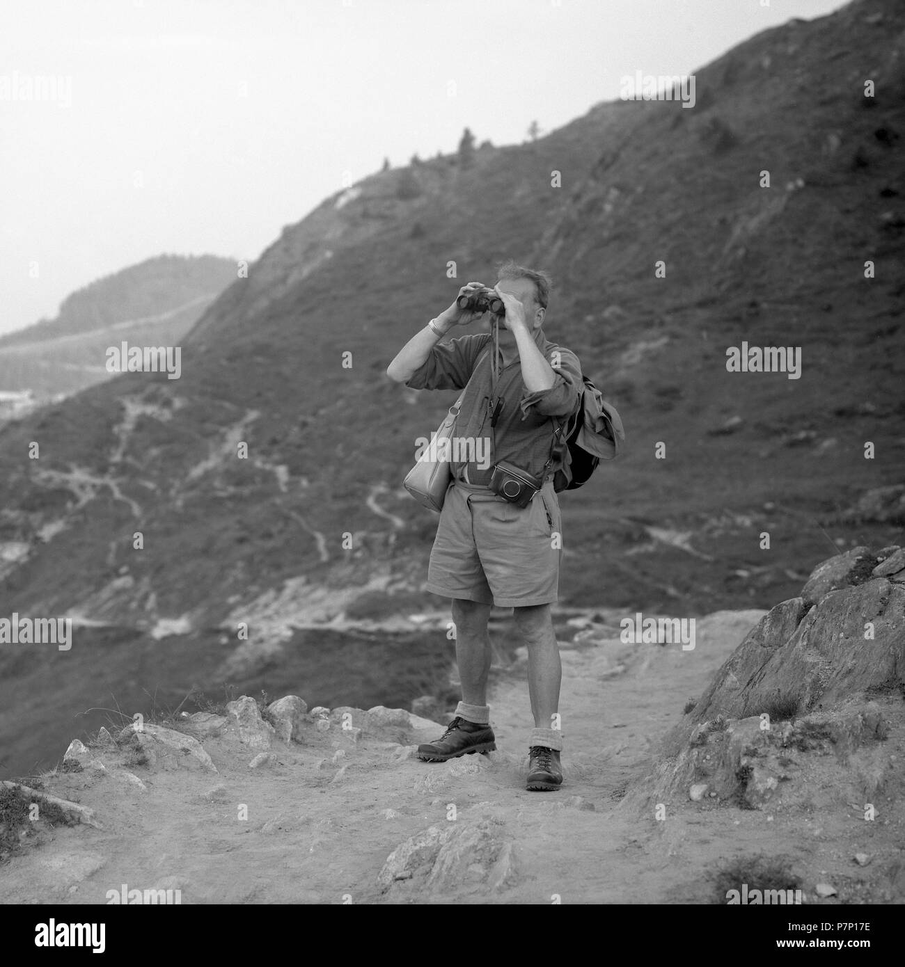 Uomo in piedi su un sentiero di montagna guardando attraverso il binocolo, ca. 1950, vicino a Freiburg, Germania Foto Stock