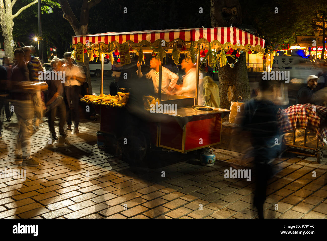 Un piccolo alimentari vendita di stallo sulla pannocchia di mais o granturco Latte (Mısır Süt) con persone passato a piedi di notte, Istanbul, Turchia Foto Stock