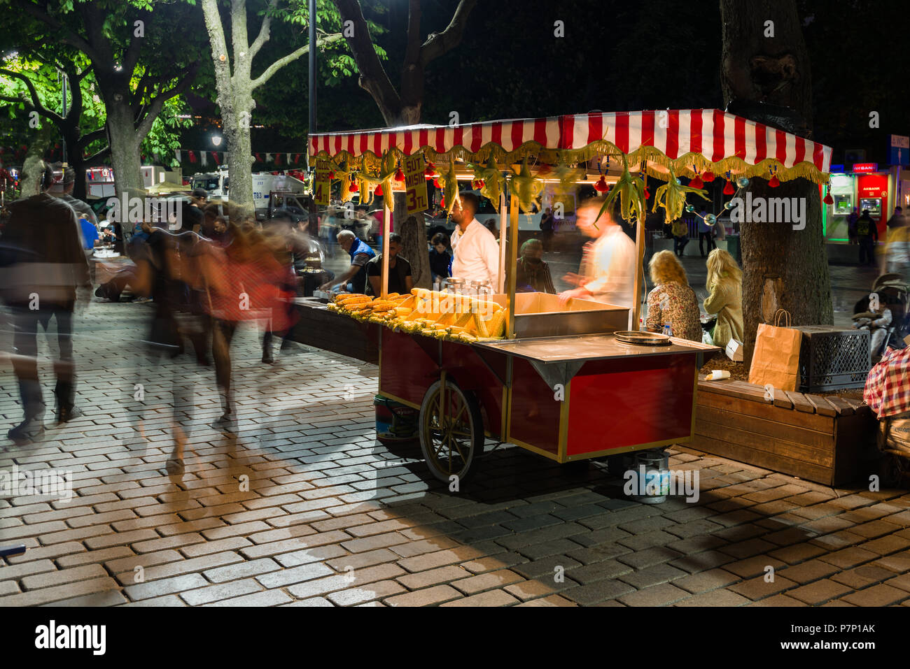 Un piccolo alimentari vendita di stallo sulla pannocchia di mais o granturco Latte (Mısır Süt) con persone passato a piedi di notte, Istanbul, Turchia Foto Stock