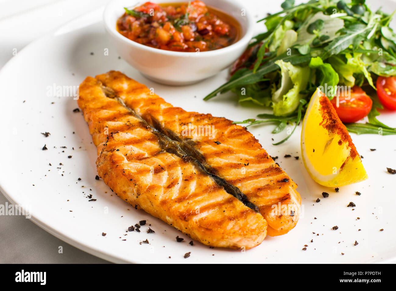 Il grande bistecca di salmone rosso pesce alla griglia con limone, salsa con verdure e verdi su piastra bianca Foto Stock