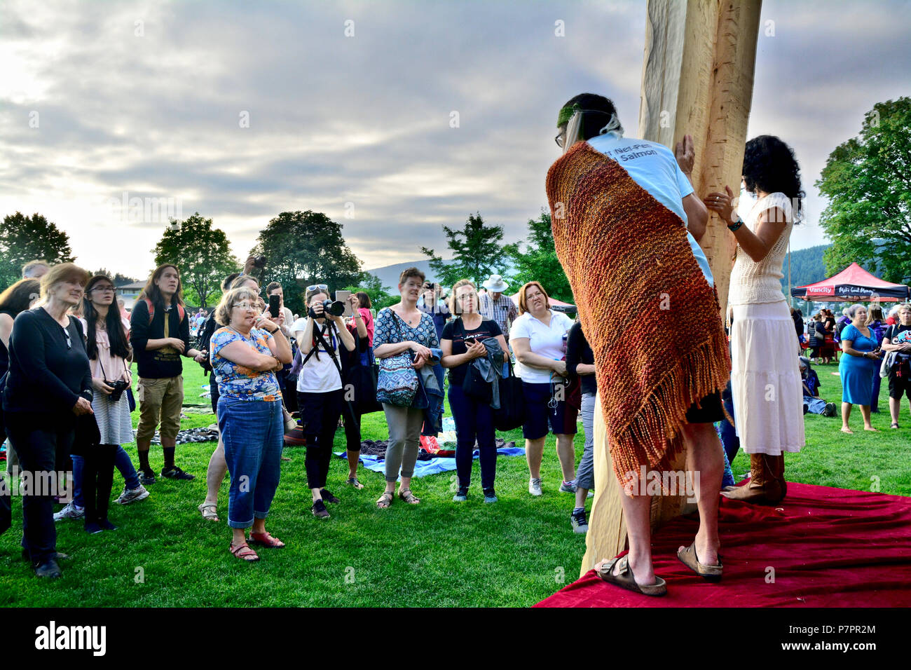 Aboriginal Carver, James Harry e sostenitori presenta il suo nuovo totem per il pubblico. Girato dal palco della prospettiva al PCT, Port Moody, BC Canada Foto Stock