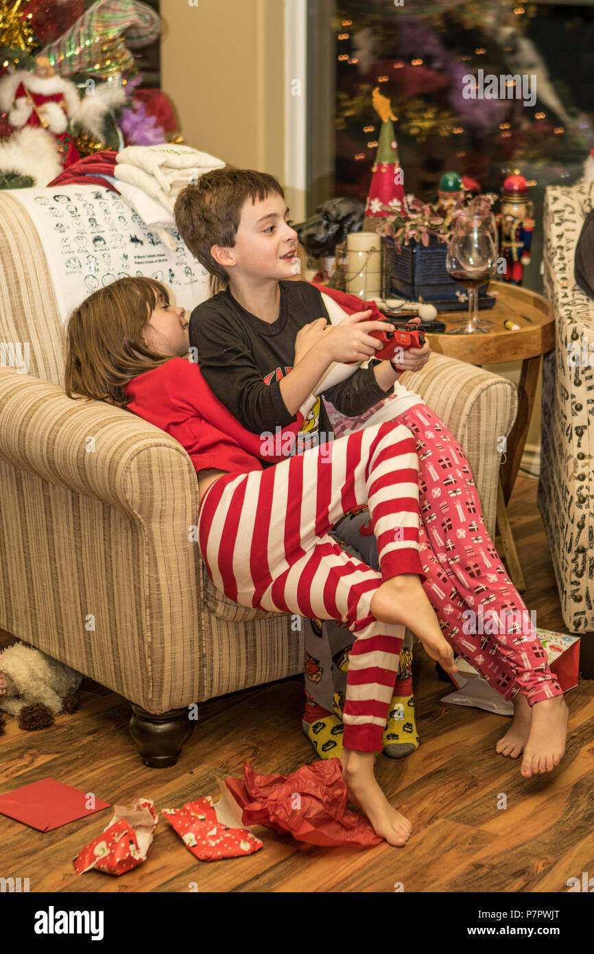Sorella e cugino, seduto nella sedia, abbracciando il fratello, di fronte al caminetto, di età compresa tra 5 e 9. Cranbrook, BC, Canada. Modello rilasciato da sinistra a destra-#104#10 Foto Stock