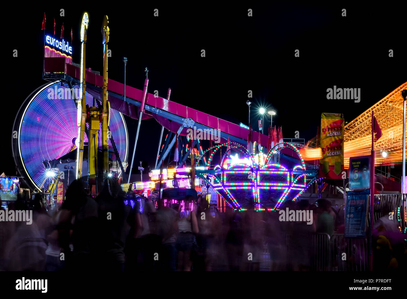 Colorate, motion-Ferris​ sfocata ruota e altre corse e spettrale di persone a Calgary Stampede a metà strada si trova nella città di Calgary, Alberta, Canada. Foto Stock