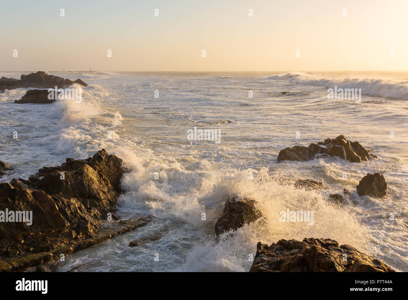 Tempestose onde che si infrangono sulla costa rocciosa al tramonto Foto Stock